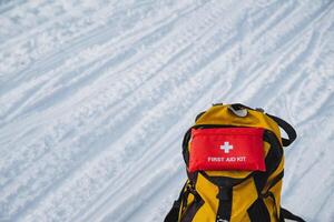 A vibrant yellow backpack features a prominently placed red first aid kit attached to it, making it not only stylish but also practical for any excursions or outdoor adventures photo