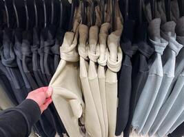 A person is holding a shirt right in front of a carefully arranged row of various shirts, showcasing different styles and colors that evoke a sense of fashion and individuality photo
