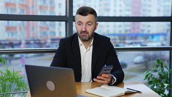 Man in a jacket and suit talk to someone on the laptop and holds a smartphone. call to the partners in office. Negotiations via laptop. video