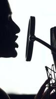 silhouette de magnifique femme est en chantant une chanson dans de face de une microphone dans un l'audio enregistrement studio sur une blanc Contexte. fermer verticale video