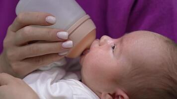 Infant babe is being fed by his mum from a bottle. Kid suckling milk from the bottle and slowly falling asleep. Close up. video