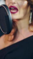 une talentueux femme avec brillant maquillage est en chantant dans une microphone dans un l'audio enregistrement studio. chanteur est profiter en chantant. fermer verticale video