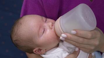 Beautiful newborn boy resting in mother's hands and being fed from a bottle. Little child closing eyes and gradually falling asleep. Close up. video