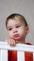 Adorable toddler boy playing with pacifier standing in the cot. Baby sits and disappears in the crib. Low angle view. Vertical video