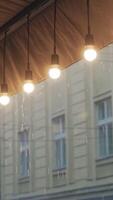 view on a row of burning light bulbs from the roof of a restaurant on the background of raindrops from the street. It's raining Vertical video