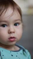 Cute grey-eyed child with adorable plump cheeks looking at camera. Baby looking down at cord in his hand. Close up. Blurred backdrop. Vertical video