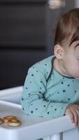 Nourishing baby boy sitting in the chair. Mom is shoving the full spoon to a boy but he is distracted by something else and turned away. Vertical video