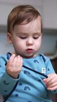 Calm peaceful baby boy is playing with a cord. Cute toddler stretching the shoe lace. Low angle view. Close up. Blurred backdrop. Vertical video