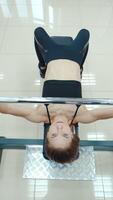 Athletic woman is lying and doing the bench press using the barbell on a white background in the gym. View from above. Endurance exercise Vertical video