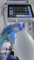 Inflating ambu bag hanging in the surgery room. Screen with life signs from a lung ventilator machine at backdrop in blur. Vertical video