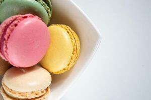 Top view of small multi-colored macaroons in a white plate on a white background photo