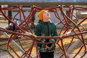 A child wearing a yellow cap climbs an alpine trellis on a playground photo