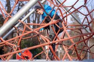 A child climbs up an alpine grid in a park on a playground on spring day photo