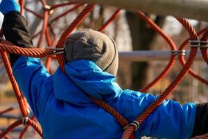 View of a boy in a blue jacket on the ropes at the playground photo