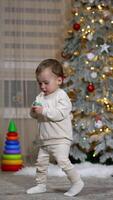 Adorable toddler stepping by the room holding a pacifier. Kid stops at the sofa. Christmas tree at backdrop. Vertical video