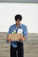 Young professional reflecting on career change while carrying a box of personal items from the office. photo