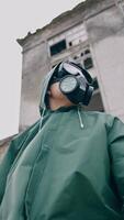 Woman in respirator and protective coat. Survivor on the background of ruined building without windows, Chemical pollution in the city. View from below. Vertical video