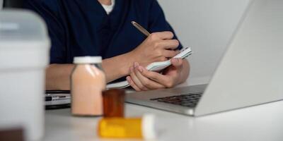 Medical student taking notes while studying medications at a desk with a laptop. photo