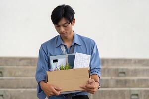 Young man leaving office with personal belongings in a box after resignation, reflecting on career transition. photo