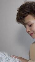 Handsome brunet boy holds a soft fluffy pillow in his hands. Teenager bends to put his head on the pillow. Close up. Light backdrop. Vertical video