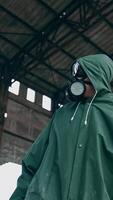 Human in a respirator and a hood is standing in abandoned building. Survivor on the background of a ruined building with holes on roof. Vertical video