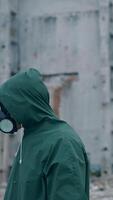Human survivor standing alone in ruined place. Guy in the gas mask and safety clothes against the background of abandoned building. Apocalypse concept. Vertical video