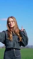 Young female blogger using a phone on field. Attractive girl leading her blog page through the mobile phone on nature background. Vertical video