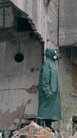 Survivor in abandoned place with radiation. Virologist man in protective costume and respirator gas mask stands in a deserted industrial factory background. Vertical video