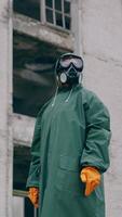 Man in protective clothing and a gas mask is standing on the background of ruined building. The concept of a post-apocalyptic world. Vertical video