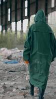 Person in abandoned place with garbage. Ecologist in protective suit walking inside the ruined building. Back view. Destructed place. Vertical video