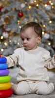 Lovely Caucasian baby building a toy pyramid. Toddler sits on the floor not far from the Christmas tree. Vertical video