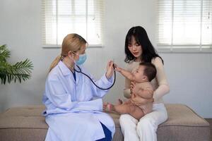 Pediatric doctor examining baby with stethoscope while parent supports child in clinic. photo