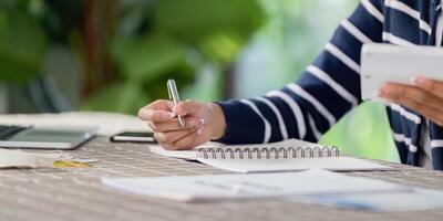 Individual writing notes for financial planning and bills while using a smartphone and notebook at home. photo