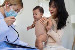 Pediatric doctor using stethoscope to examine baby while parent holds child in clinic. photo
