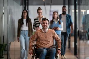 A businessman with disability in a wheelchair is surrounded by supportive colleagues in a modern office, showcasing the strength of teamwork, inclusivity, and empowerment in the face of challenges. photo
