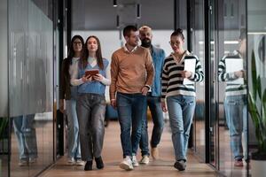 Business team in a modern open space startup office walking together. Diverse group of businesspeople smiling while having a discussion. Successful mixed race colleagues collaborating on a new project photo