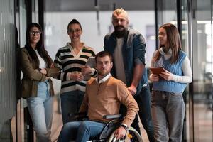 A businessman with disability in a wheelchair is surrounded by supportive colleagues in a modern office, showcasing the strength of teamwork, inclusivity, and empowerment in the face of challenges. photo
