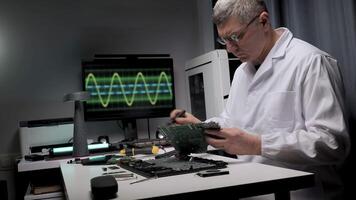 A skilled technician focuses on repairing electronic devices at a tidy workbench. Tools and equipment are organized, with a monitor displaying waveforms in the background. video
