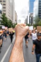 A crowd gathers in the city streets, holding signs and chanting for change. One hand is raised with a clenched fist, symbolizing unity and determination among the protesters photo