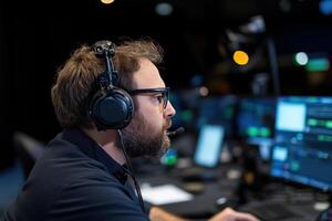 man with a beard in headphones works in a dark studio in front of equipment with monitors photo