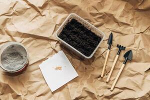 Kraft paper background, fertile soil and garden tools on top, top view. Planting seedlings in spring photo