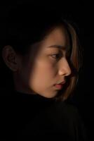 A young Asian woman, captured in profile. She has a subtle expression, with her lips closed and eyes looking slightly downward photo