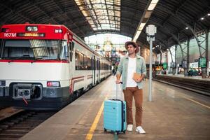 latin Tourist waiting for the train at the station holding a suitcase and a guide photo