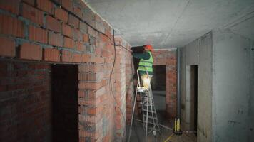 Electrician working on wiring in a building under construction, A construction worker in a safety vest and helmet installing electrical wiring on a brick wall. video
