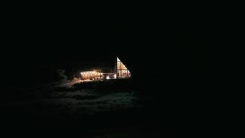 Distant night view of illuminated modern cabin surrounded by snowy landscape, peaceful remote setting. video