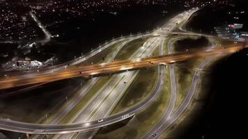 Aerial view of illuminated highway interchange at night, with flowing traffic and surrounding city lights. video