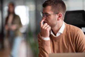 Funny scene of a businessman putting a finger in his nose. Employee in the office, thinking and brainstorming ideas for a startup. Man at workplace working on laptop, copywriting and innovation in a photo