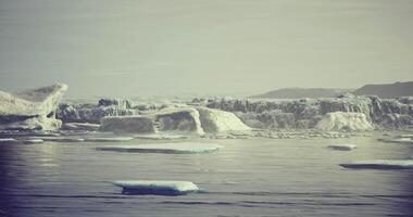 Icebergs floating in a calm sea under a soft gray sky during daylight video
