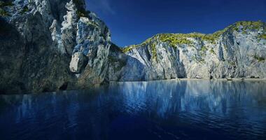 Serene blue water reflects rugged cliffs under a clear sky at midday video