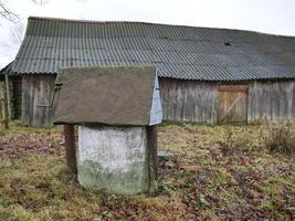 A charming, rustic well stands prominently in front of an old, weathered barn amidst a serene countryside setting photo
